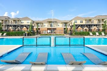 A swimming pool with lounge chairs and apartment buildings in the background.